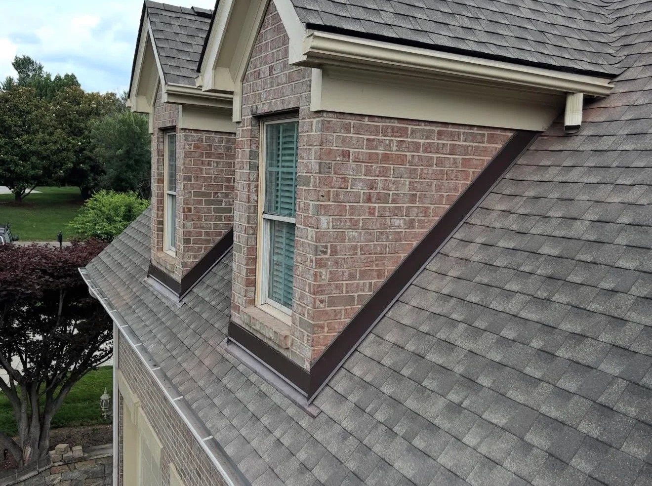 Brown metal flashing wrapping brick dormers where they meet an asphalt-shingle roof